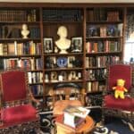 A home library with a pair of antique arm chairs in red velvet against a backdrop of books on built-in bookshelves.