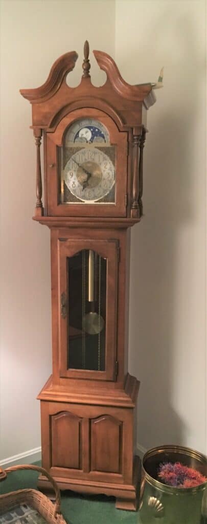 A typical light-oak colored grandfather clock with sun and moon motif at the top of the clock.