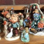 A group of at least a half dozen porcelain Hummel figurines stare into the camera lens.