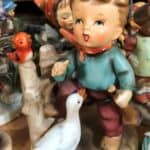 A white duck or a goose looks up at little boy in a blue shirt. It's a Hummel figurine.