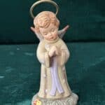 A Hummel figurine depicts an angel in the form of a little girl, with a halo over her head.