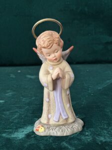 A Hummel figurine depicts an angel in the form of a little girl, with a halo over her head.