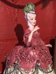 Porcelain figurine of a Victorian woman in a red dress with a green bonnet.
