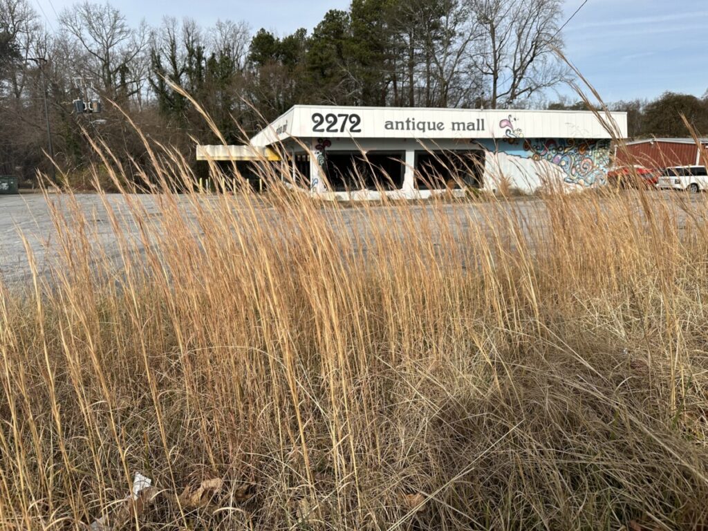 An abandoned antiques mall sits in the distance behind a dirty parking lot and a patch of weeds.