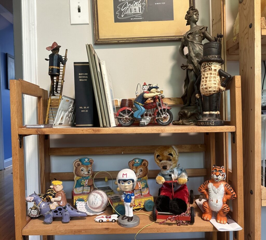 A bookshelf features popular collectibles including a cast iron Popeye figure on a motorcycle, autographed baseball, rare books, Louis Marx tin windup fireman climbing ladder, and more.