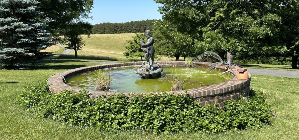 A large front yard fountain with a boy spitting out water sits on the lawn of a giant Frederick home.