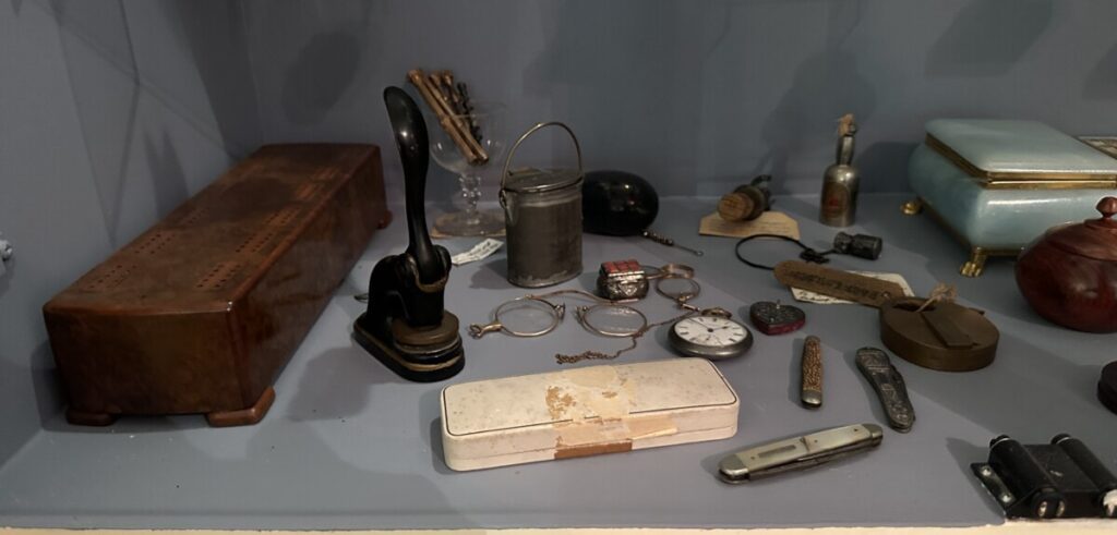 A display of antique knives and watches including pocket watches sit in a glass cabinet.