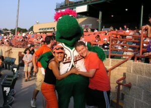 Orion's Attic co-owners Won-ok Kim, left, a big green Bowie Baysox mascot in the middle and Chris Lancette on the right. All embraced in a hug.