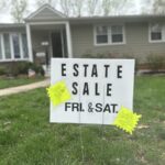 An estate sale sign staked in the ground in front of an expensive house that should have gone on the market much sooner.