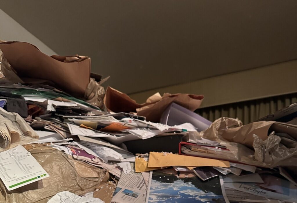 View of a hoarder house bedroom with junk mail soaring to within a few feet of the ceiling.