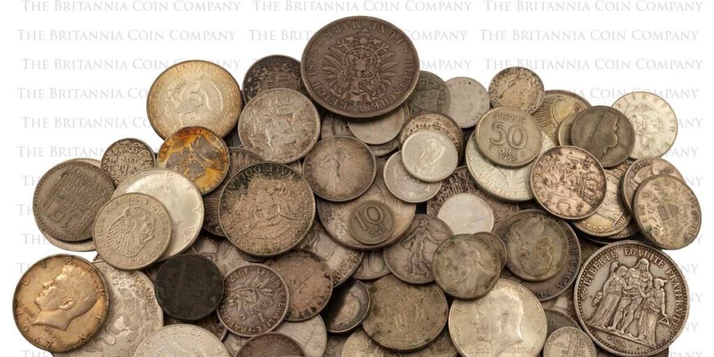 A pile of old foreign coins and some American coins scattered on a desk.