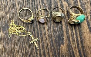 Four gold rings and a gold cross sit on a desk.