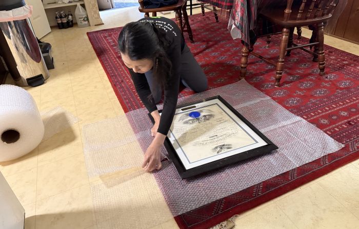 Orion's Attic co-owner Wonok Kim on her hands and knees carefully wrapping a framed president-signed document during an estate cleanout