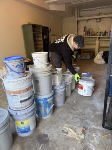 Yuck Old Paint technician organizing multiple buckets of leftover paint and household chemicals during hazardous waste cleanup.