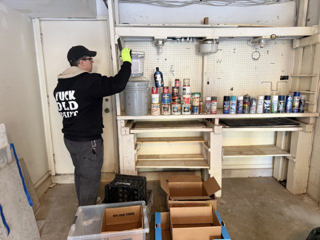 Yuck Old Paint technician sorting paint cans and household chemicals during hazardous waste cleanup.