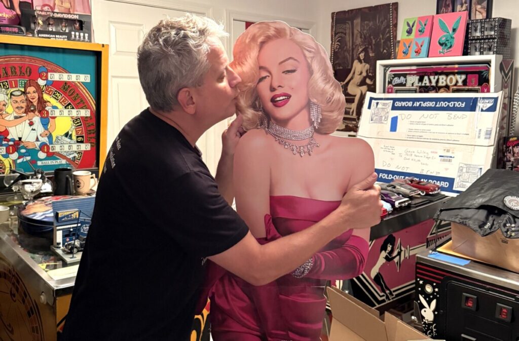Orion's Attic co-owner Chris Lancette in black t-shirt playfully kisses cardboard cutout of Marilyn Monroe.