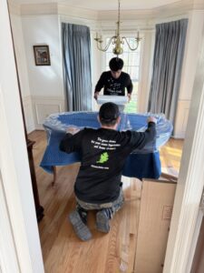 Orion's Attic crew members wrap a dining table with blankets and plastic wrap as part of our moving services.