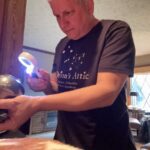 Orion's Attic owner Chris Lancette in black company t-shirt examines an item with a magnifying glass.