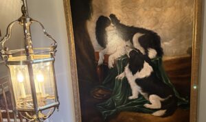 Oil on canvas painting of one dog looking up toward another.