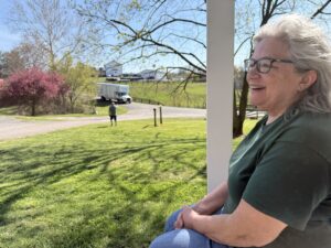 Client Diana, with her back to the exterior of her new house, looks on with relief as the second Orion's Attic moving truck pulls up.