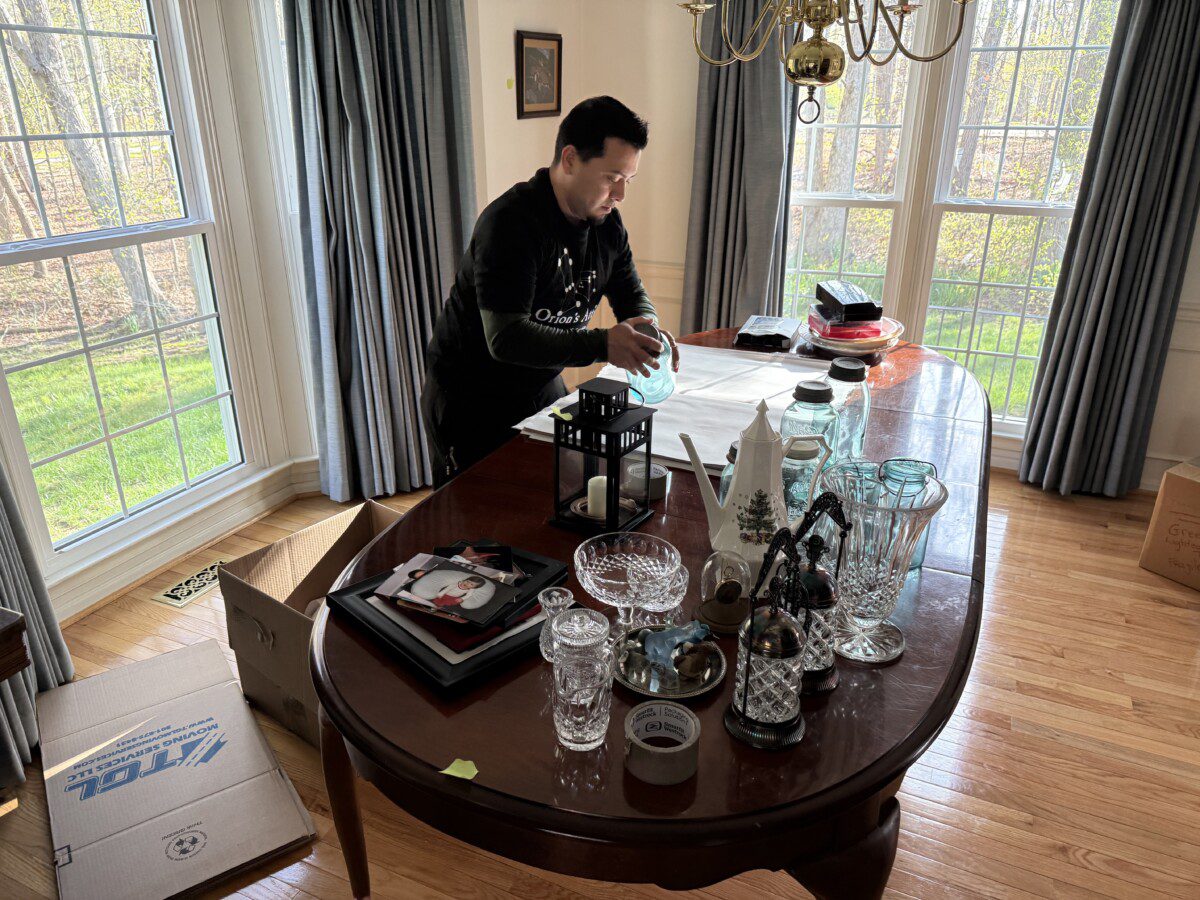 An Orion's Attic mover carefully packs glasses and other fragile items gathered on a kitchen table.